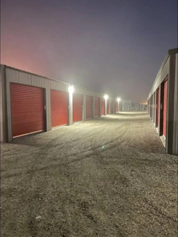 Lit storage unit drive aisle at dusk with red roll-up doors on both sides